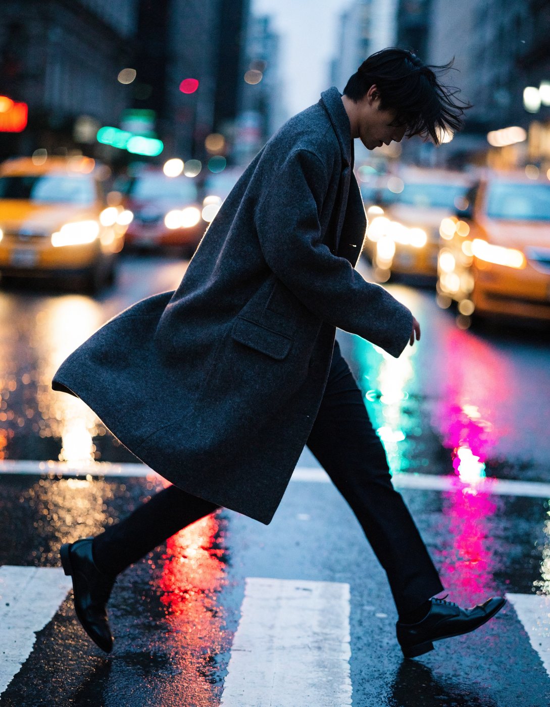 Street style figure crossing a wet city street at blue hour